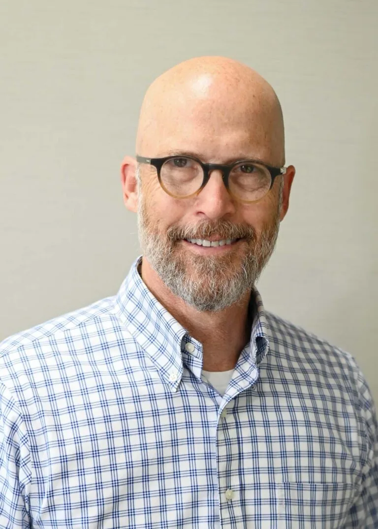 Headshot of Dr. James Boggs wearing a blue and white checkered shirt with a plain light-colored background.
